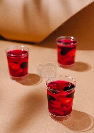 Three glasses of red berry mocktails on a warm beige background with playful shadows