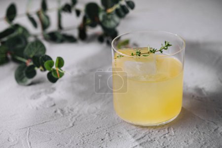 Delicate herbal cocktail with ice, garnished with fresh thyme, against a clean backdrop