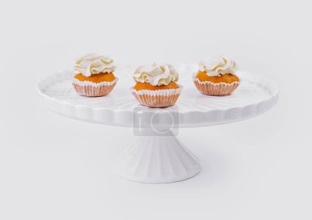Drei leckere Cupcakes mit cremigem Belag auf einem klassischen weißen Kuchenständer vor weißem Hintergrund