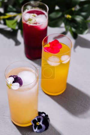 Zwei bunte Cocktails mit essbaren Blumen an einem hellen, sonnigen Tag