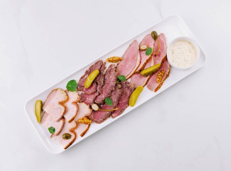Elegant serving of sliced deli meats with pickles and mustard on a white platter