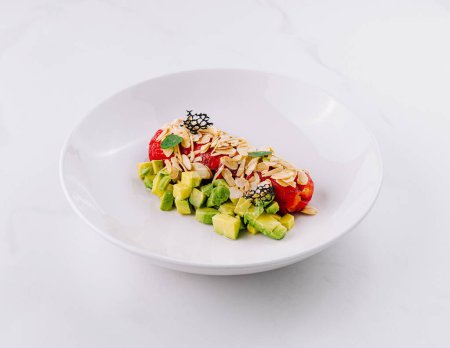 Fresh avocado salad with bell pepper and nuts and slivered almonds on a white plate