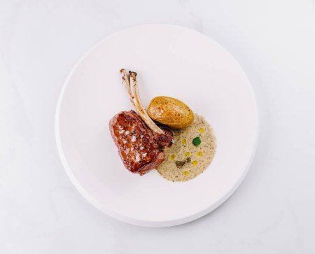 Elegant plating of a juicy lamb chop with golden roasted potatoes on a white background