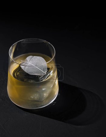 Artistic image of a whiskey glass with ice and decorative silver leaf on a dark background
