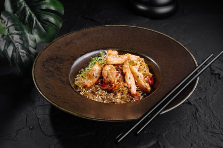 Nouilles asiatiques sautés aux légumes et poulet servies dans une assiette marron élégante avec baguettes