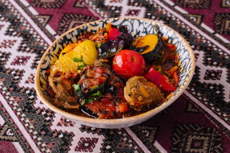 Guiso de uzbek salado con verduras y hierbas mixtas, servido en un tazón decorativo sobre un mantel estampado