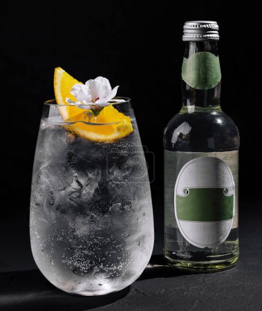 Elegante ginebra y bebida tónica adornada con rodaja de limón y flor sobre fondo oscuro