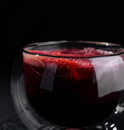 A modern double-walled glass cup filled with red tea, isolated on a dark, moody backdrop