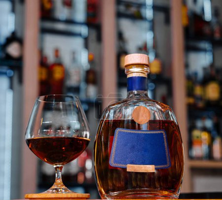 Premium bottle of brandy beside a filled snifter glass presented on a vibrant bar counter with blurry shelves of bottles in the background