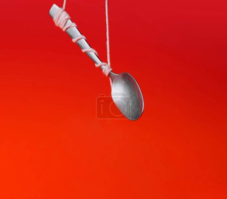 Silver spoon tied with string against a vibrant red backdrop, creating an illusion of floating