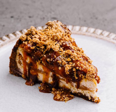 Single slice of rich caramel cheesecake topped with crunchy nuts, presented on an elegant plate