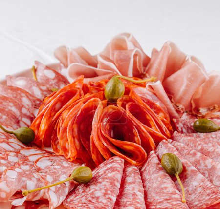 Tentadora selección de carnes curadas adornadas con alcaparras, presentadas en un plato elegante