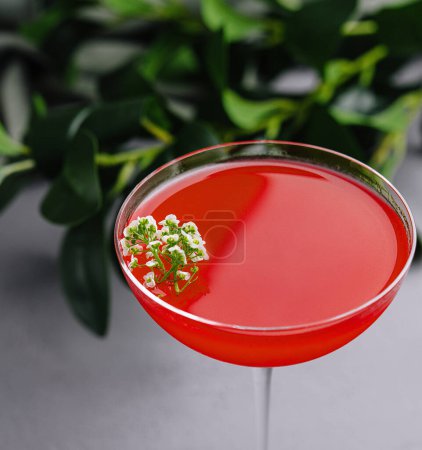 Vibrant red cocktail in a stemmed glass, adorned with white flowers, presented on a sleek surface