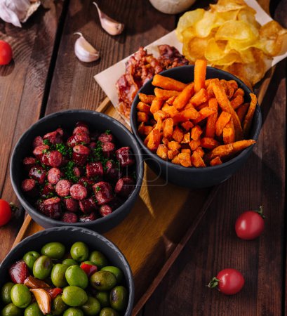 Vibrant spread of tapas including green olives, spicy sausage, and seasoned fries