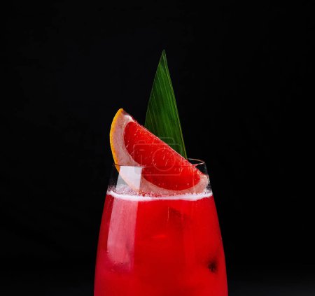 Elegant red cocktail garnished with grapefruit and leaf on a dark background