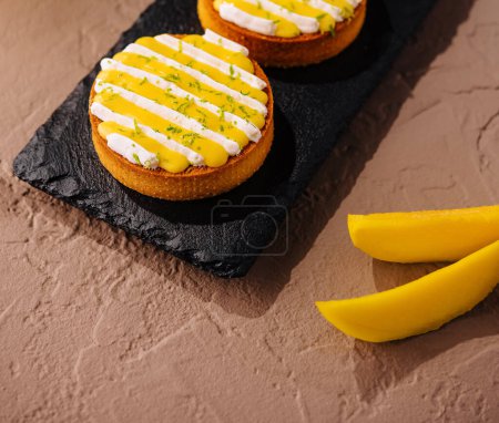 Three delicious mango tarts with creamy topping and lime zest, elegantly served on a slate board
