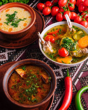 Hearty bowls of homemade soup with fresh vegetables and herbs on an ethnic tablecloth