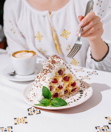 Téléchargez les photos : Gros plan d'une femme sur le point de manger du gâteau à partir de crêpes roulées avec de la crème et une tasse de café en arrière-plan - en image libre de droit