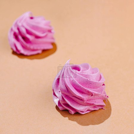Two delicate pink meringue swirls artistically placed on a warm peach-colored backdrop