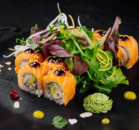 Sushi roll z żywymi dodatkami i zieloną sałatką serwowane na stylowej czarnej płycie łupkowej na ciemnym tle