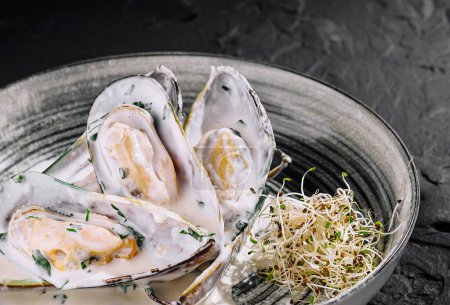 Delicate mussels smothered in a creamy sauce, garnished with sprouts, presented on a stylish plate against a dark background