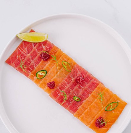 Top view of a plate of salmon carpaccio garnished with lime and jalapeo slices