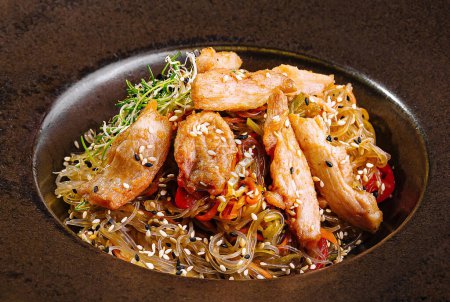 Asiatische Rührnudeln mit Gemüse und Hühnchen in einem stilvollen braunen Teller serviert