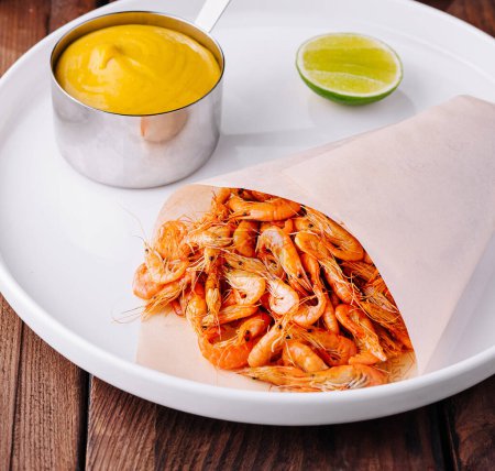 Delicious plate of cooked shrimp served with golden sauce and lime, presented on a rustic wooden table