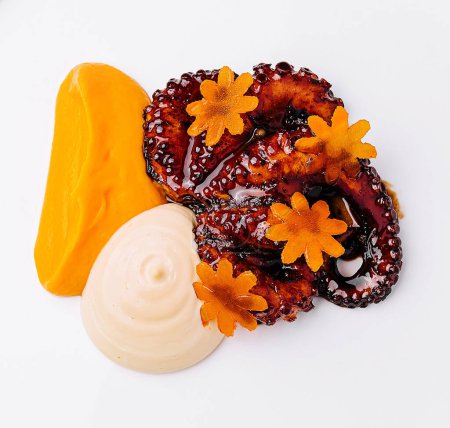 Zarter Oktopussalat mit kunstvoller Karottengarnitur, serviert auf einem glatten weißen Teller vor grauem, strukturiertem Hintergrund