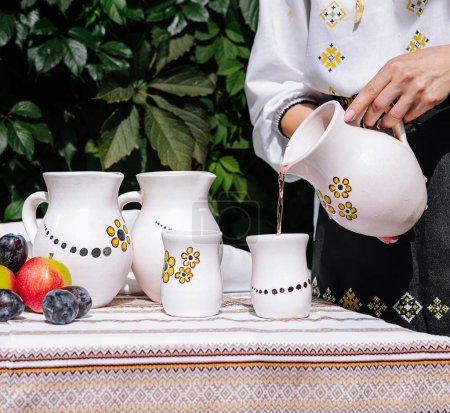 Person serviert ein Getränk aus einem Keramikkrug in eine Tasse auf einem Tisch mit ethnischem Dekor