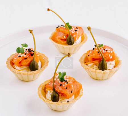 Delicious tartlets filled with smoked salmon and garnish on a sleek white plate