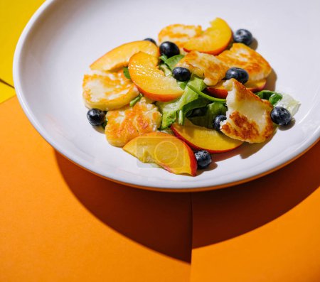 Halloumi- und Pfirsichsalat mit Blaubeeren auf weißem Teller mit zweifarbigem Hintergrund