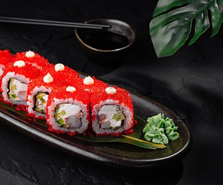 Elegant sushi roll covered with red caviar, served with soy sauce and wasabi on a sleek black plate
