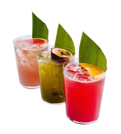 Three colorful tropical drinks adorned with fruit slices and leaves against a white background
