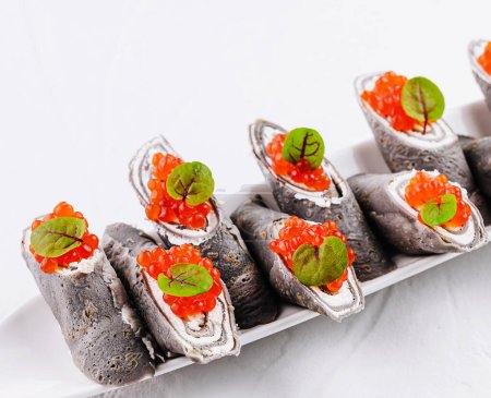 Elegant black crepe rolls filled with cream cheese and topped with red caviar and fresh herbs