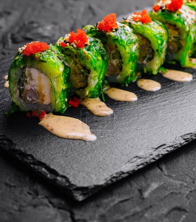 Appetizing sushi roll garnished with tobiko, served on a slate board with wasabi and ginger