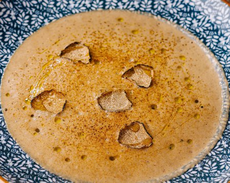 Elegant bowl of smooth, blended soup garnished with truffle slices, on textured background