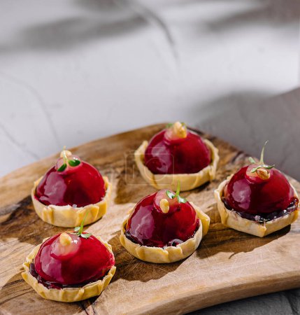 Artistic display of raspberry tarts and a layered beverage on a rustic wooden serving board