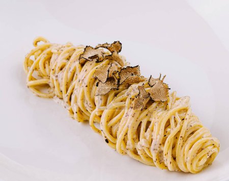 Elegant serving of spaghetti topped with shaved truffles on a sleek plate, marble background