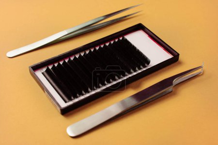 High-precision tweezers and eyelash strips for extensions, showcased on a vibrant yellow surface