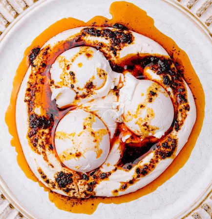 Photo for Top view of delicious poached eggs drizzled with a spicy sauce, served on an ornate white plate - Royalty Free Image