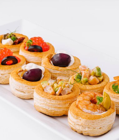 Selection of elegant mini tartlets with savory toppings on a sleek white platter