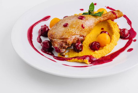 Elegant presentation of duck confit on a bed of creamy puree with vibrant berry sauce