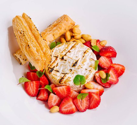Exquisita y elegante presentación gourmet de queso barbacoa con hojaldre dulce plateado y fresas frescas en un plato blanco. Presentado en una vista superior sobre un fondo de mármol