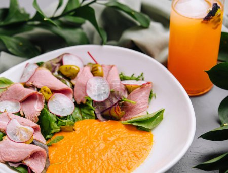 Vibrant dish of roast beef salad with colorful dressing, served with a refreshing orange juice