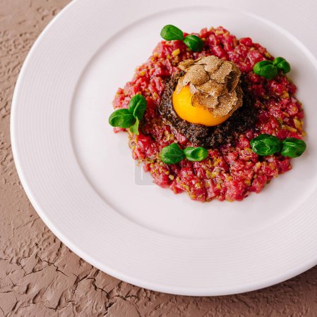 Elegant beef tartare topped with a quail egg and black truffle, served on a white plate