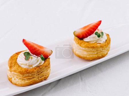 Delicious puff pastry desserts with cream and fresh strawberries on a sleek white plate