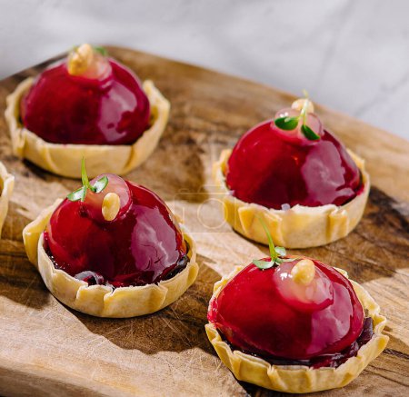 Gourmet raspberry tarts with glossy glaze on a rustic wooden serving board