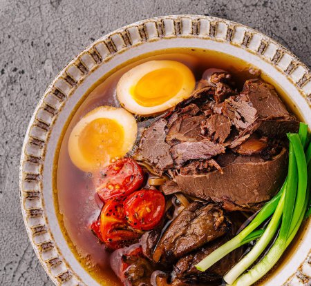 Traditional beef ramen with soft-boiled egg, tomatoes, and green onions in a rich broth