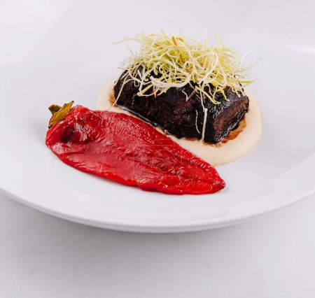 Elegante plato de ternera tierna estofada en una mancha de puré con una vibrante guarnición de verduras rojas en un plato blanco